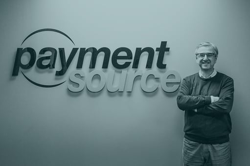 George DeMarchi proudly standing in front of the Payment Source logo in the Toronto Payment Source office